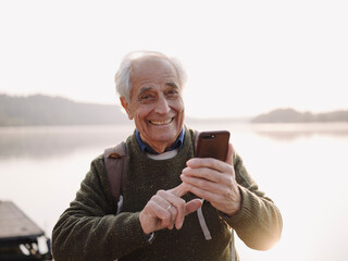 Smiling senior man using mobile phone while standing against sky