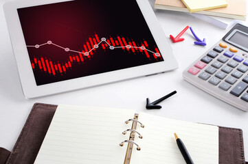 Depressing downtrend graph on computer digital tablet on busy working desk. Economic crisis concept...