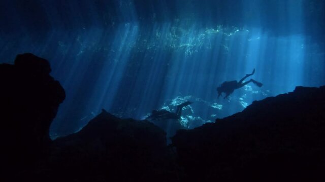 Divers swimming in a cenote with light rays. Divers in a cave. Clear water diving. Elden Cenote