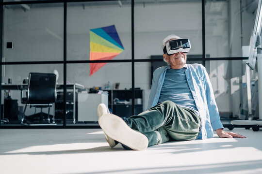 Businessman using virtual reality headset while relaxing on floor in office