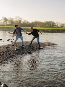 Father and son throwing pebbles in river during autumn