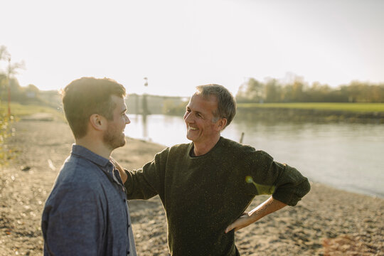 Smiling father giving advice to son at riverbank