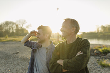 Smiling son searching while standing by father on riverbank at evening