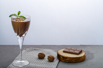 Chocolate cocktail with nuts and mint in a glass on a blue background near nuts and chocolate on a napkin.