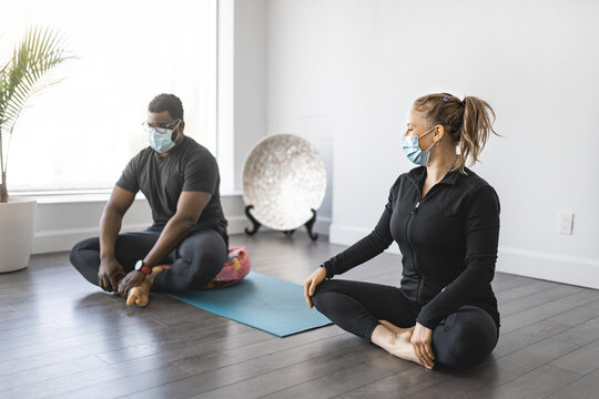 Personal Trainer Doing Yoga Pose In Sunny Studio With Client Wearing Mask