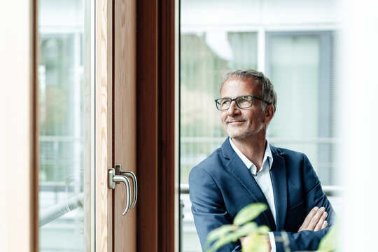 Smiling male business professional looking through window in office