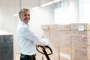 Smiling senior businessman holding pallet jack in warehouse
