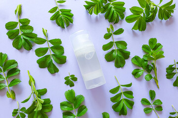 Transparent bottle of intimate lubricant gel and fresh green leaves on light purple backgroundl....