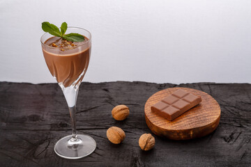 Chocolate cocktail with nuts and mint in a glass near chocolate and nuts on a black background.