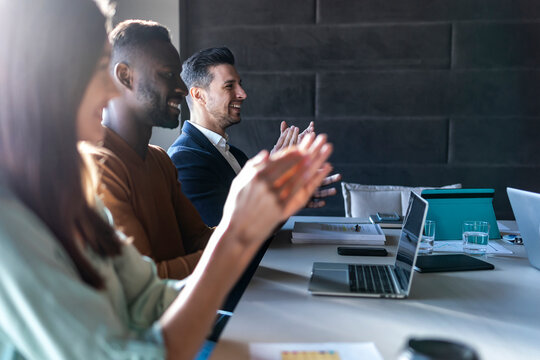 Smiling business people applauding while sitting in meeting at office