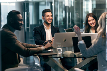 Smiling colleague looking at businesswoman while sitting in meeting at office