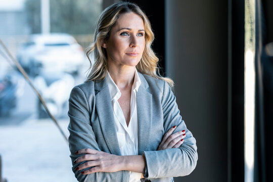 Thoughtful businesswoman looking away while standing with arms crossed in office