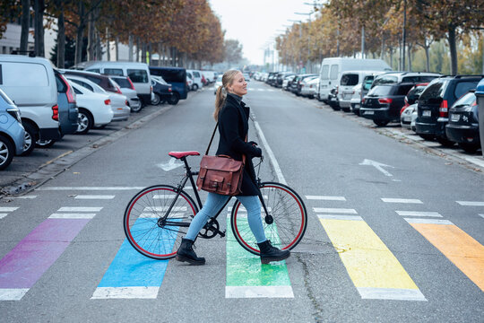 Woman with bicycle walking on zebra crossing while looking away