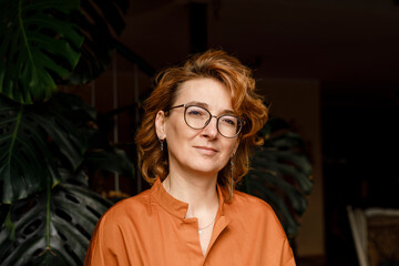 Confident mature woman with eyeglasses against plants at home
