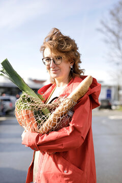Smiling woman holding mesh bag with groceries while standing outdoors