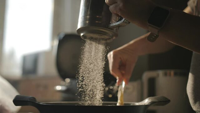 A woman prepares dough for baking in the kitchen. Close-up of sifting flour with a metal sieve into the dough being stirred in a saucepan.
