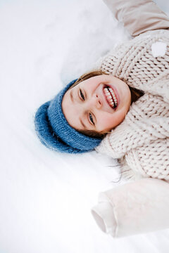 Cheerful girl with scarf lying on snow during winter