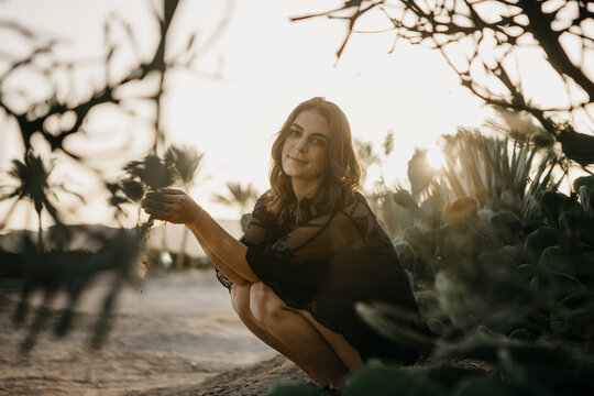 Smiling woman with sand crouching by cactus plant during sunset