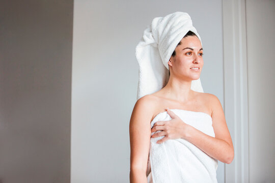 Beautiful woman in towel looking away while standing by wall - Powered by Adobe