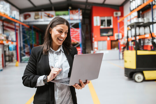 Smiling female manager using laptop in illuminated distribution warehouse