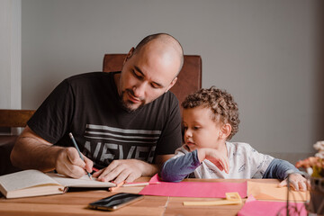 Dad writing in the diary while his son watches carefully what he does