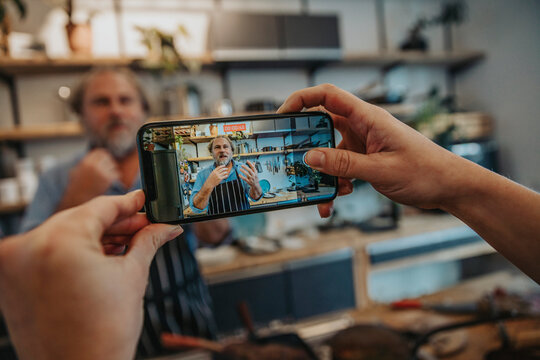 Woman filming chef through mobile phone while standing in kitchen