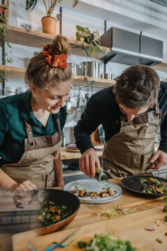 Chef team garnishing food plate with herb sauce while working in kitchen
