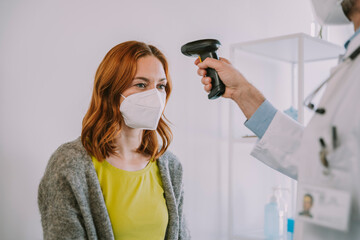 Doctor checking patient temperature through infrared thermometer while standing in examination room
