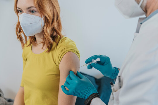 Doctor injecting COVID-19 vaccination on patient hand while standing at examination room