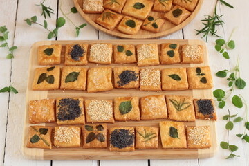Homemade crackers decorated with herb leaves, sesame seeds, poppy seeds and salt