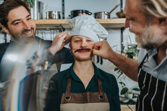 Chefs having fun with young colleague while standing in kitchen
