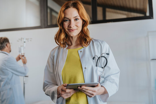 Female doctor holding digital tablet while standing with coworker in background at clinic