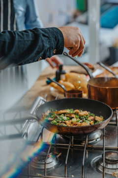 Chef sprinkling vegetable leaf over food in frying pan while standing by colleague in kitchen