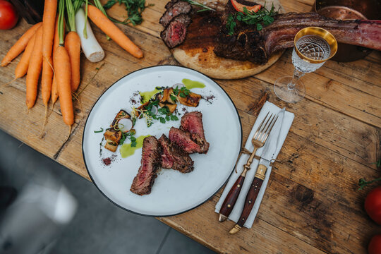 Tomahawk Steak Garnished With Cooked Vegetable In Plate On Kitchen Island