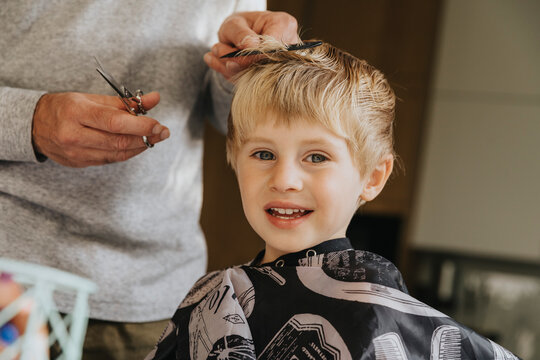 Blond boy smiling when getting haircut from father at home