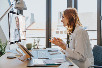 Healthcare worker talking to coworker on video call over computer while sitting at office