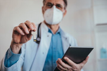 Doctor holding USB stick and digital tablet while standing in clinic