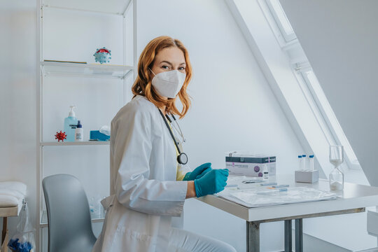 Female doctor wearing protective face mask siting by desk at examination room