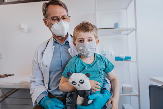 Doctor And Patient Wearing Protective Face Mask While Sitting At Clinic