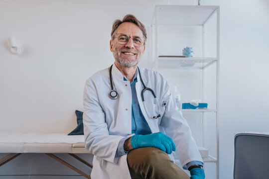 General practitioner with protective glove smiling while sitting in clinic