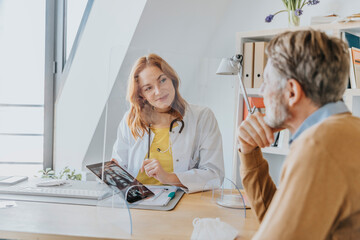 Female doctor explaining patient over x-ray while sitting by screen partition at doctor's office