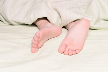 Legs sticking out from under the blanket close-up. The concept of sleep, insomnia or sound sleep, lullaby