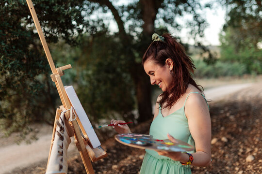 Young woman artist painting on easel