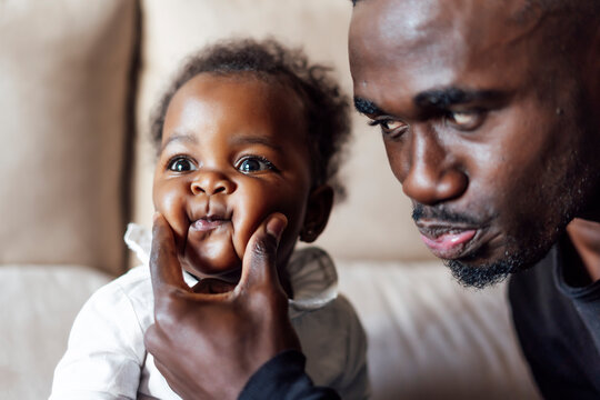 Playful father squeezing baby girl's cheeks at home