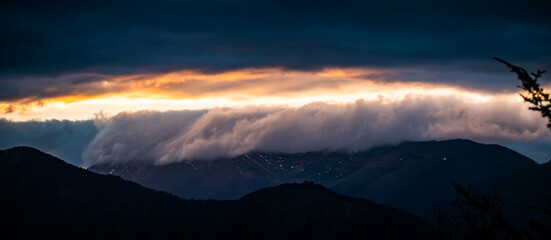 Sea of clouds flowing above mountains at sunset