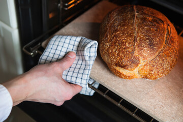 Man taking out homemade wheat warm bread from the oven holding kitchen towel in hand