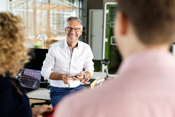 Smiling male business professional holding digital tablet while discussing with colleagues in office