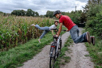 Mature man with daughter jumping while leaning in bicycle at agricultural field