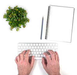 top view of person typing on wireless computer keyboard on white desk with potted plant and notepad with pencil