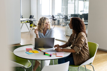 Businesswomen with laptop discussing at table in open plan office